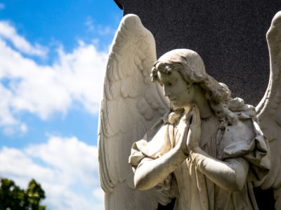 Low Angle View Of Angel Statue In Cemetery Against Cloudy Sky