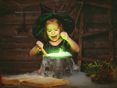 Halloween. little witch child cooking potion in the cauldron with spell book